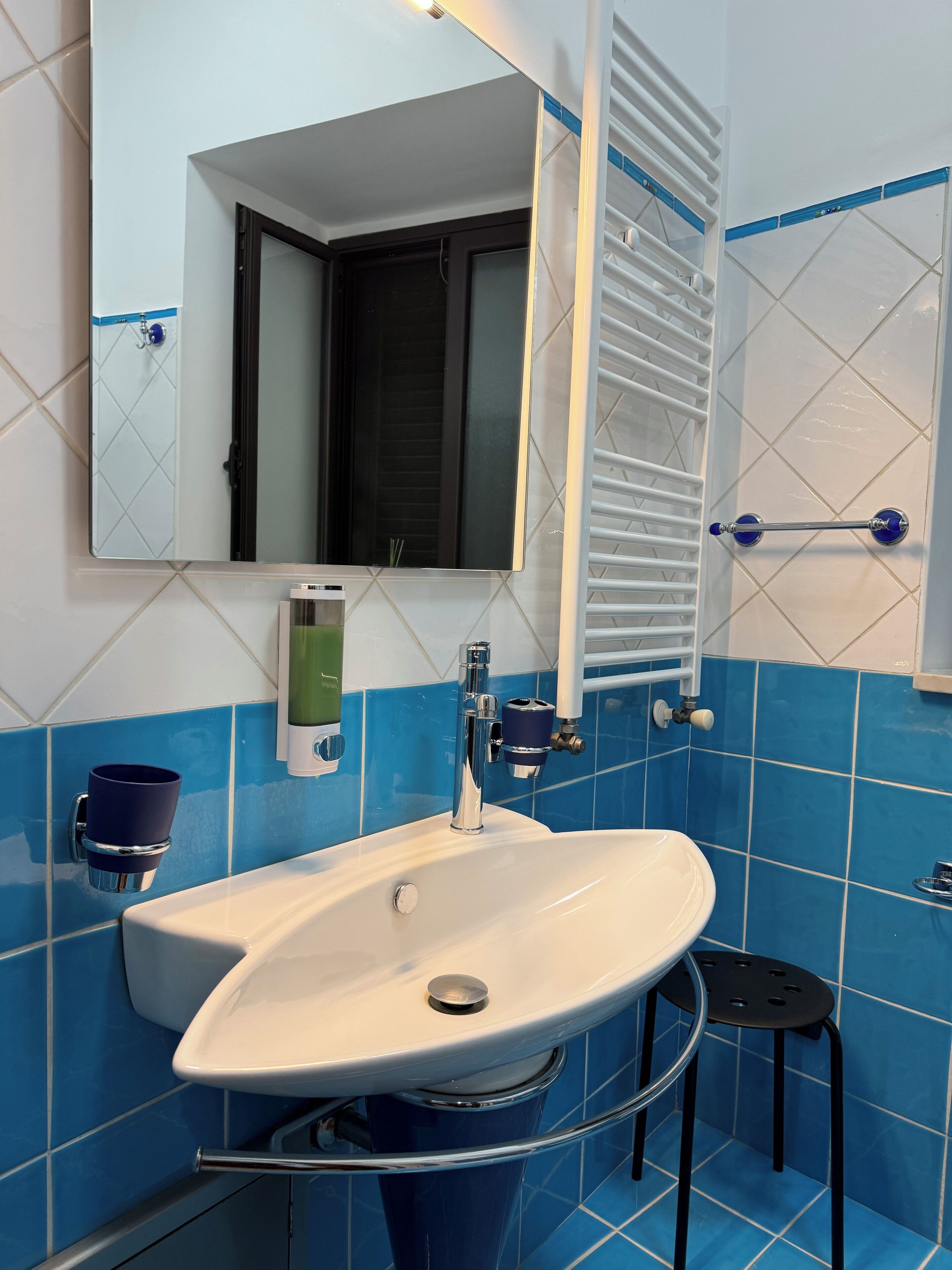 Un baño con un lavamanos blanco, un espejo, un perchero para toallas y una pared con azulejos azules.