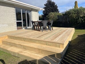 A wooden deck with a table and chairs, leading to a glass door entrance.