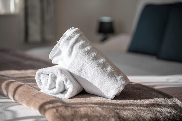A neatly folded white towel on a brown blanket on a bed.