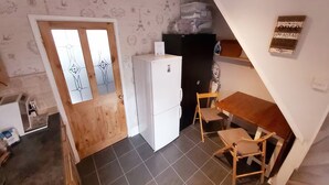 Cocina compacta con refrigerador blanco, puerta de madera y piso de baldosas.