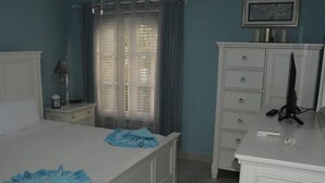 Een slaapkamer met een bed, nachtkastje, dressoir en een raam met gordijnen.