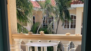 Een balkon met een witte tafel en stoelen, omgeven door witte balustrades en palmbomen.