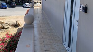 Een hotelgangen met een betegelde vloer, een witte muur met een deur en een balkon met uitzicht op de straat.