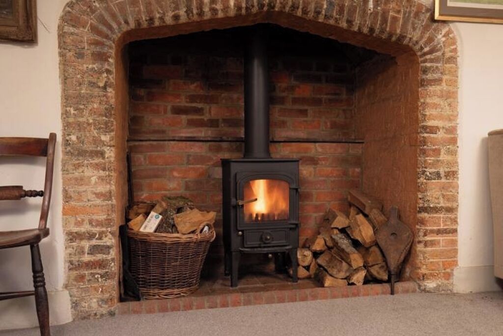 A brick fireplace with a black wood-burning stove, a wicker basket, and a stack of firewood.