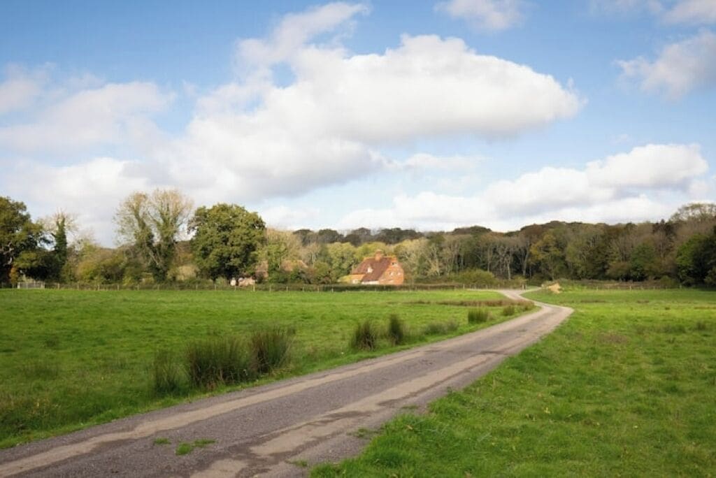 Una strada di campagna che serpeggia attraverso un prato verde con una casa all'orizzonte.