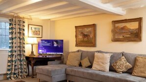 A living room with a grey sofa, a television, and two framed paintings on the wall. - Grade 2 Listed Rural Farm House (Chiddingfold)