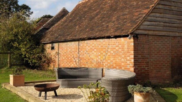 A brick building with a sloped roof, a fire pit, outdoor seating, and a garden area. - Grade 2 Listed Rural Farm House (Chiddingfold)