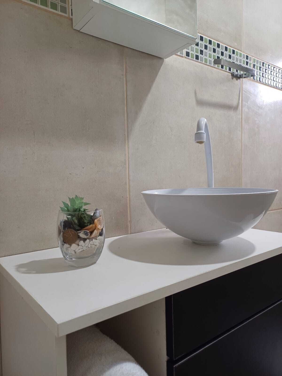 A bathroom with a white sink, a glass bowl with decorative stones and a plant, and a tiled backsplash.