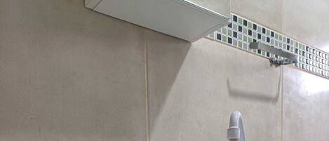 A bathroom with a white sink, a glass bowl with decorative stones and a plant, and a tiled backsplash.