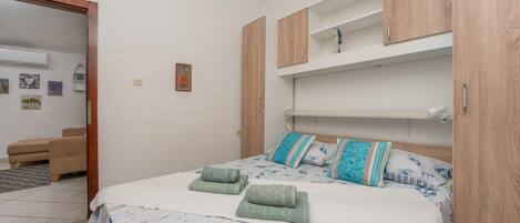 A bedroom with a bed, a wooden wardrobe, and a small seating area.