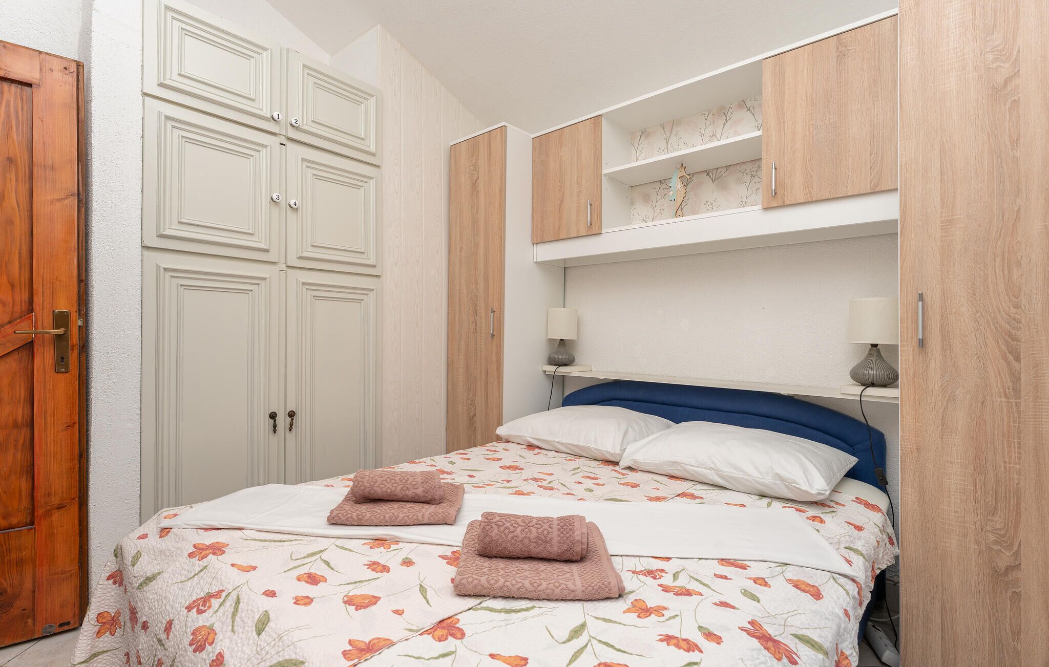 A bedroom with a bed, two nightstands, a wooden wardrobe, and a door.