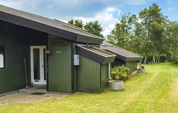 A row of green cabins with a number '109' on the door, a small garden area, and a clear sky.