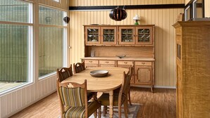 Ein Esszimmer mit Holzboden, ausgestattet mit einem runden Tisch, Stühlen, Holzschränken und einem Fenster mit Jalousien.