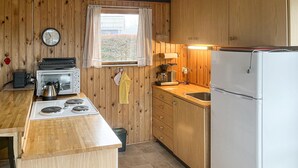 Eine kleine Küche mit Holzwänden, einem Herd, einem Toaster, einer Kaffeemaschine und einem Kühlschrank.