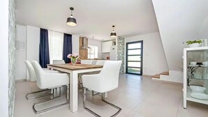 Une cuisine moderne avec des meubles blancs, un plan de travail en bois et un coin repas comprenant une table et des chaises blanches.