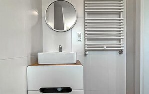 Casa de banho moderna com lavatório branco, espelho redondo e porta-toalhas.