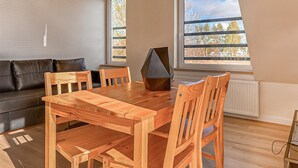 A modern living room with a wooden dining table, chairs, a black geometric coffee table, a grey sofa, and large windows with a view of trees. - Awesome apartment in Trzesacz with swimming pool (Trzesacz)
