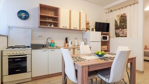A compact kitchen with a gas stove, oven, microwave, and a refrigerator. There is a dining table with chairs and a bowl of fruit.