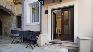 A building with a sign indicating it is a studio apartment. There are two chairs and a table outside, and a door with a window.