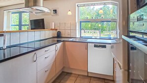Une cuisine compacte avec des meubles blancs, un plan de travail noir, une fenêtre donnant sur un espace verdoyant et un lave-vaisselle encastré.