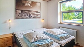Une chambre avec deux lits, une table de chevet, une lampe fixée au mur, une fenêtre donnant sur un paysage verdoyant et un tableau au-dessus des lits.