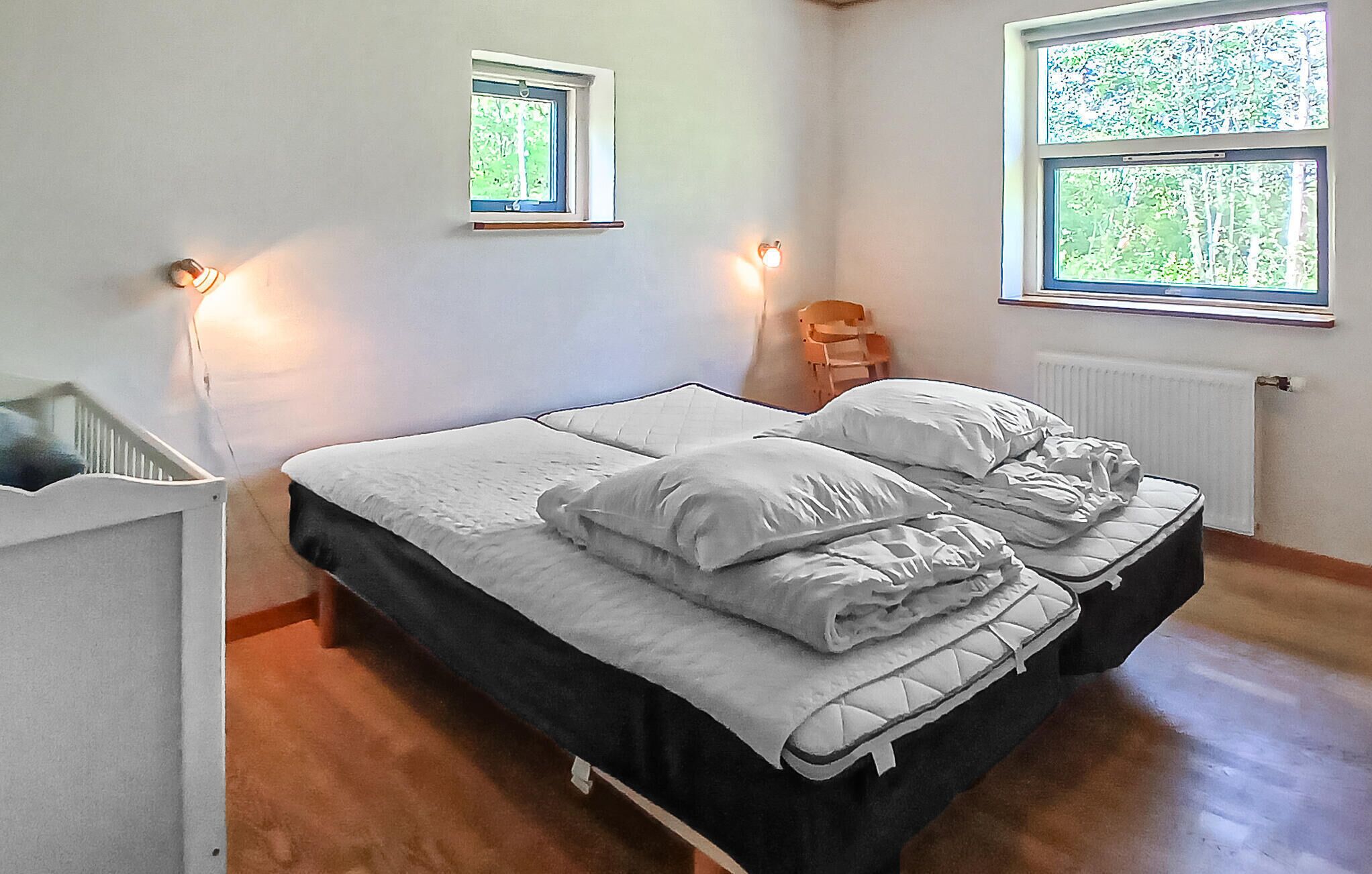 Ein Schlafzimmer mit einem Doppelbett, zwei Nachttischen, einem Heizkörper und zwei Fenstern.