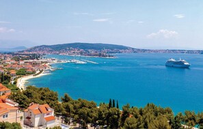 A coastal town with a large cruise ship in the bay, surrounded by residential buildings and a clear blue sea.