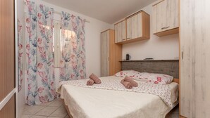A bedroom with a bed, floral curtains, a wooden headboard, and a small shelf with a kettle. - Cozy apartment in Pakostane with WiFi (Pakostane)