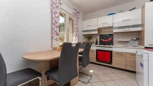 A compact kitchen with a dining area, featuring a wooden table, grey chairs, and a red towel hanging on the oven. - Cozy apartment in Pakostane with WiFi (Pakostane)