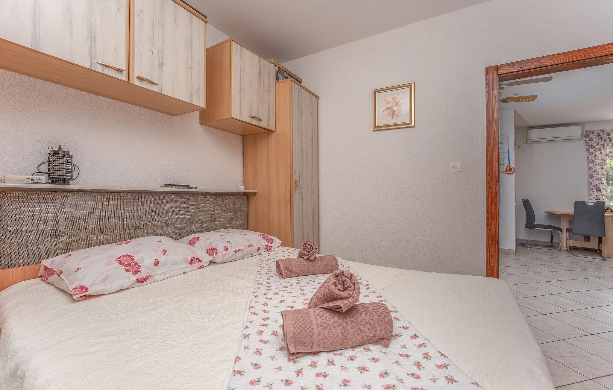 A bedroom with a bed, wooden cabinets, a headboard, a framed picture on the wall, and a view of a dining area.