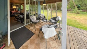 An outdoor patio with wicker chairs and a small table, a wooden deck, and a glass door leading to an interior space with a dining table and chairs.