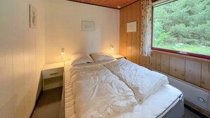A bedroom with a bed, two bedside tables, a window with curtains, and a view of greenery outside.