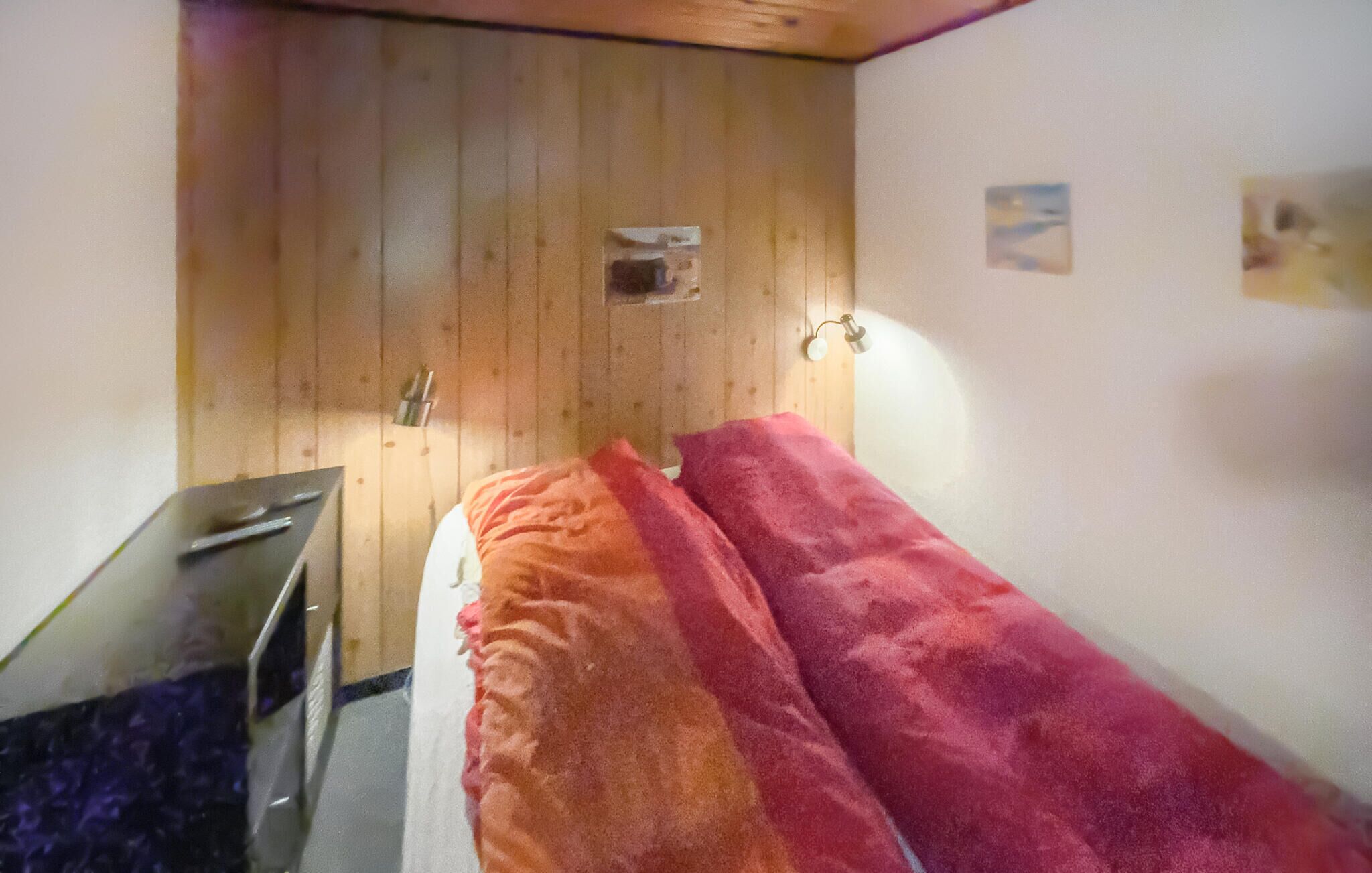A small, single-bed room with a wooden wardrobe, a desk, and a wall-mounted lamp.