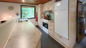 A kitchen with a built-in oven, a refrigerator, and a window with a view of greenery.