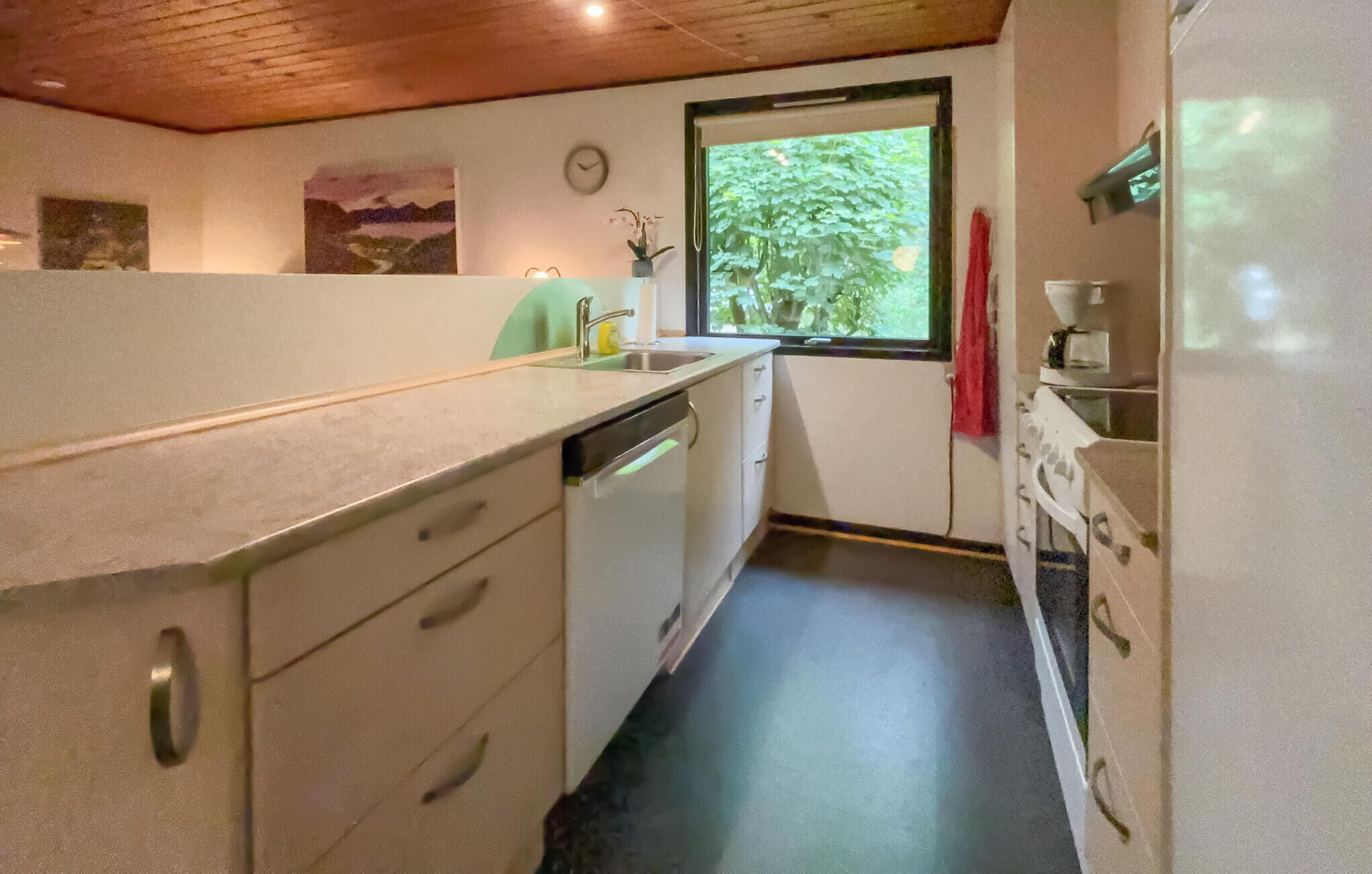 A compact kitchen with white cabinets, a sink, and a window with a view of greenery.