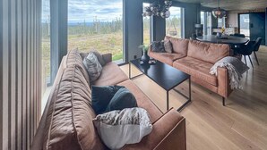En moderne stue med en brun lædersofa, et sort sofabord, og et spiseområde med et stort bord og stole.