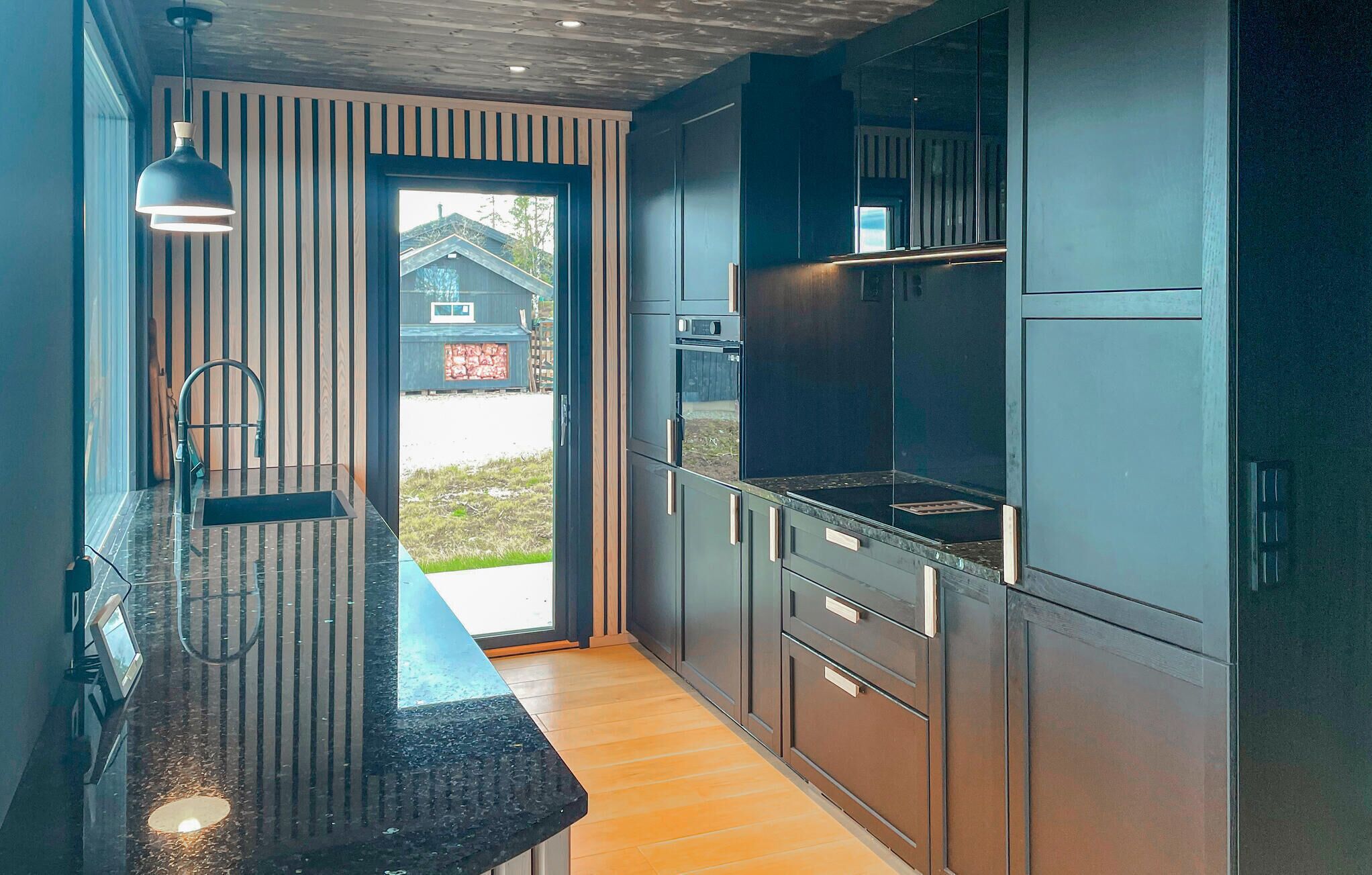 Une cuisine moderne avec des meubles de couleur sombre, un plan de travail noir et une fenêtre donnant sur l’extérieur.