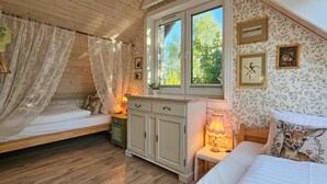 A cozy bedroom with a wooden ceiling, a bed with a canopy, a nightstand, a dresser, and a window with a view of greenery.