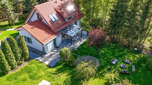 A two-story house with a red roof, a glass conservatory, and a well-maintained garden with outdoor furniture.