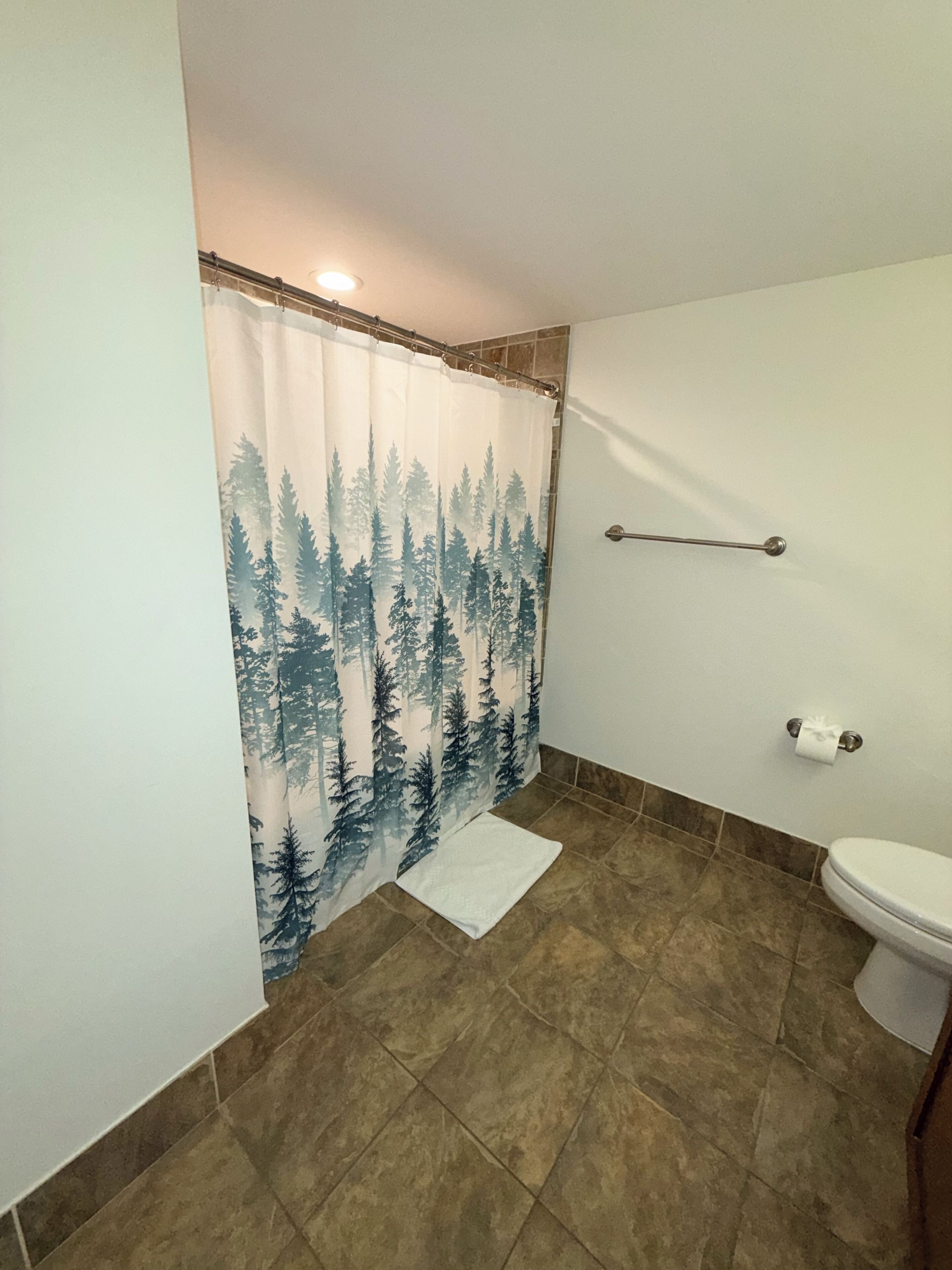 Ein Badezimmer mit Duschvorhang mit Waldmuster, einer Toilette und braunen Fliesen.