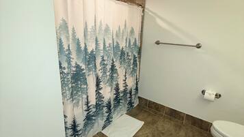 Ein Badezimmer mit Duschvorhang mit Waldmuster, einer Toilette und braunen Fliesen.