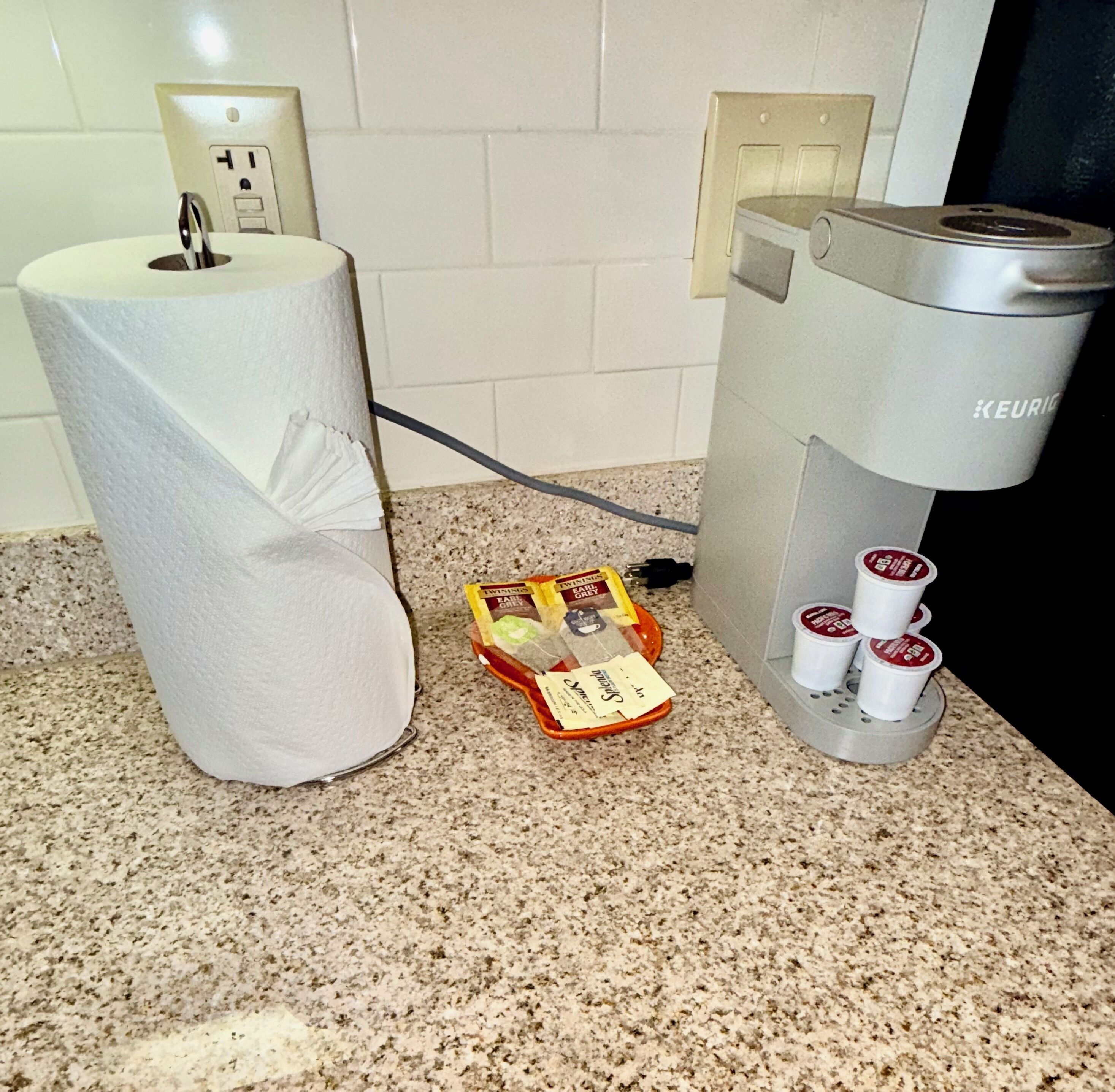 A kitchen with a paper towel dispenser, a coffee maker, and a basket of coffee pods.