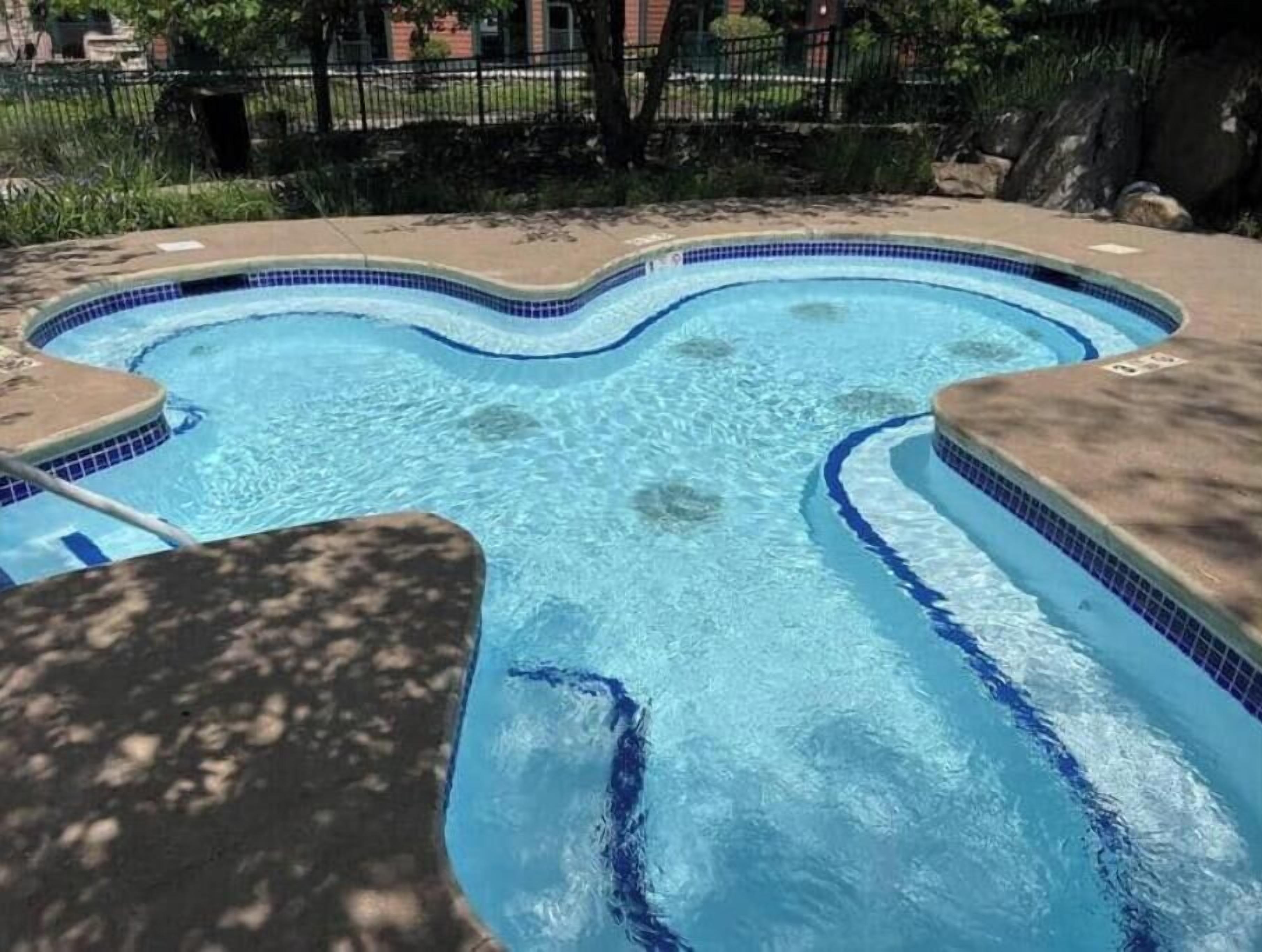 Une piscine dont le bord présente un motif ondulé, entourée d’une terrasse carrelée et d’une bordure en pierre.