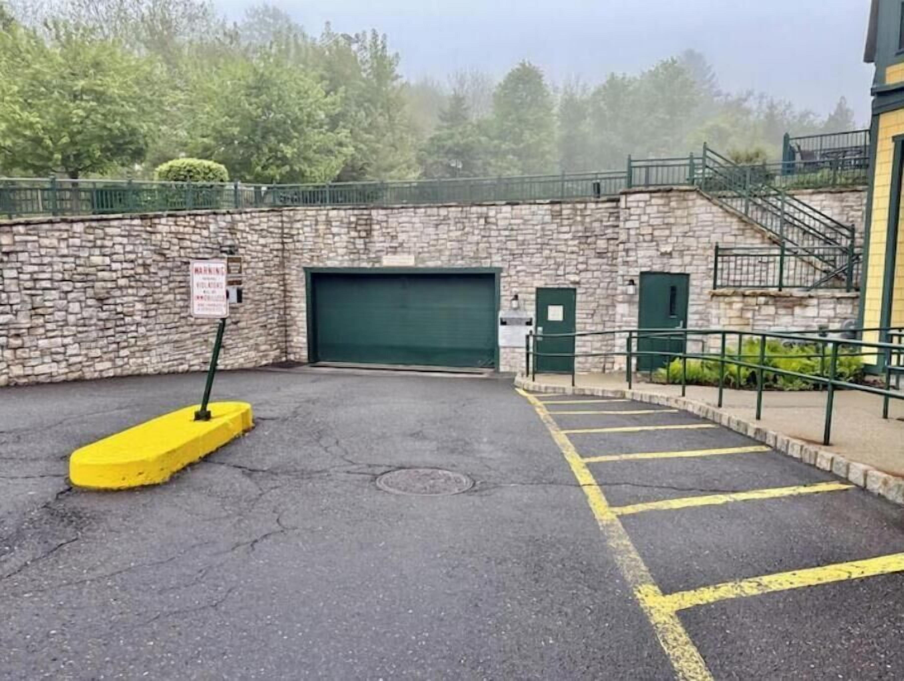 Un'area di parcheggio con un muro in pietra, un portone del garage verde e linee gialle per i parcheggi.