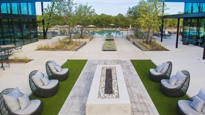 A poolside area with wicker chairs, a central fire feature, and glass buildings. - Cozy Apartment in Austin by The Key Rentals (Austin)