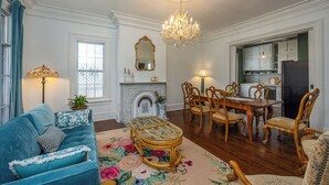 Un salon spacieux avec un canapé bleu, une table à manger en bois et des chaises, un lustre et une cheminée.