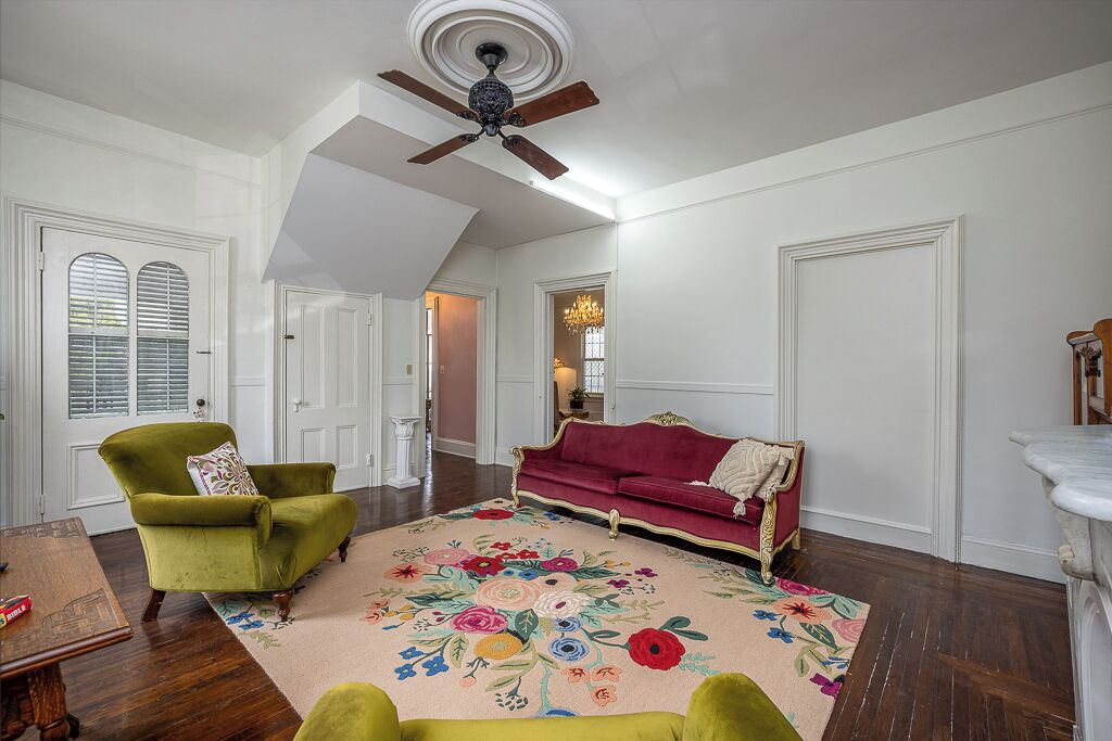 A spacious living room with a high ceiling fan, a floral rug, a green armchair, a red sofa, and a wooden coffee table.