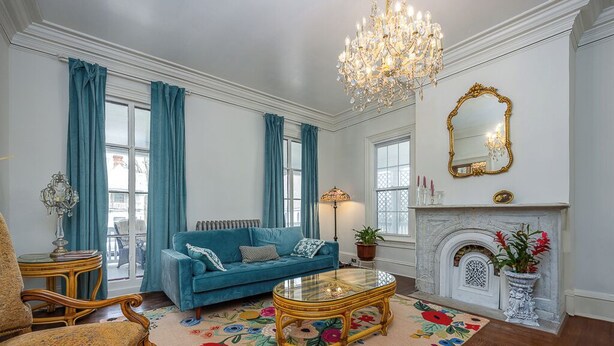 Une pièce avec un canapé bleu, une table basse en verre, un lustre, une cheminée et un miroir au mur.