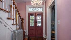 Un couloir avec un escalier en bois, une porte rouge et un lustre.