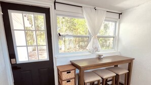 Ein Zimmer mit Schreibtisch aus Holz, zwei Stühlen, einem Fenster mit Vorhängen und einer Tür mit Fußmatte.